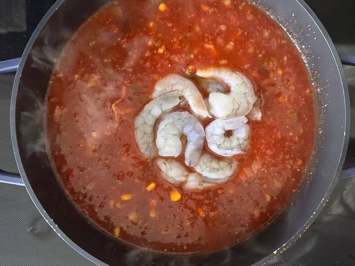 Raw shrimp being added to the tortilla soup near the end of cooking.