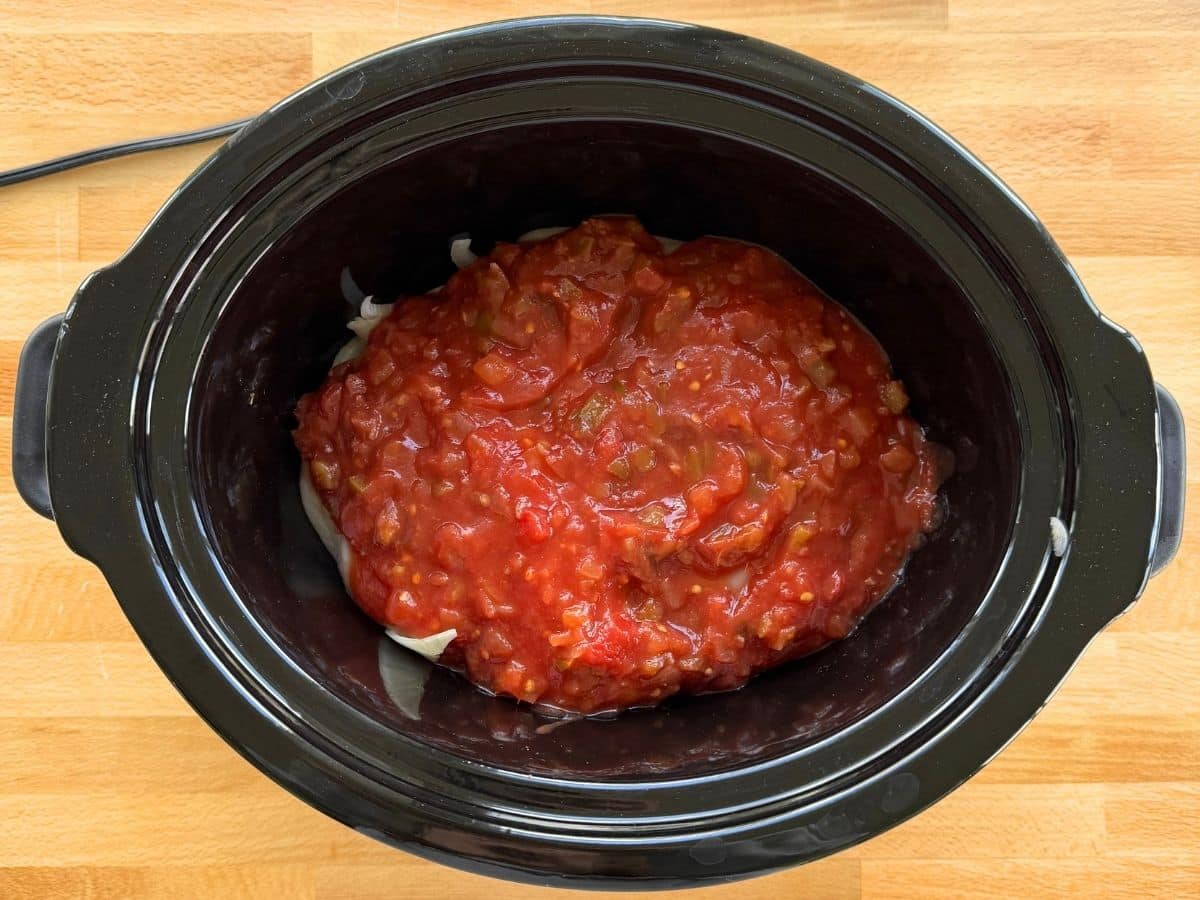Chicken breasts and sliced onions topped with chunky salsa in a slow cooker.