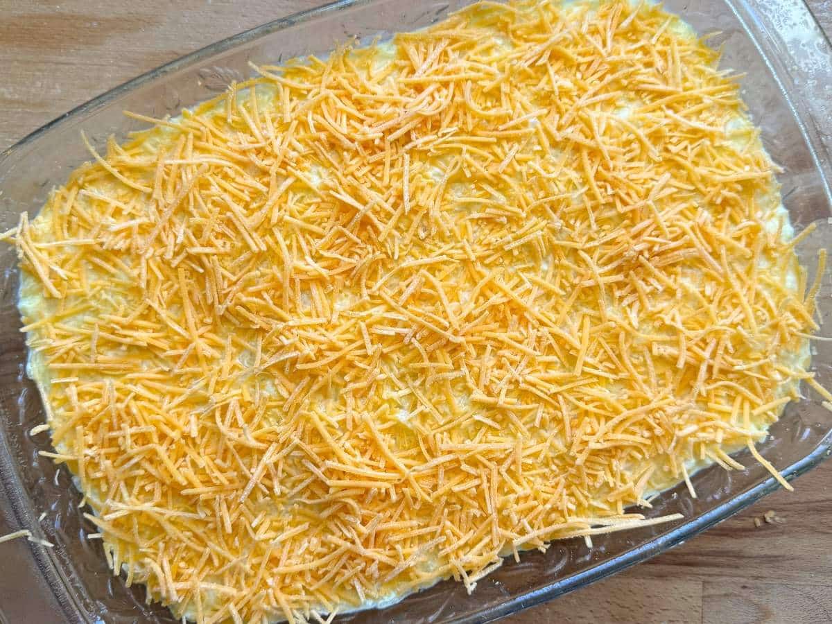 Unbaked spaghetti squash au gratin topped with shredded cheddar cheese in a casserole dish.