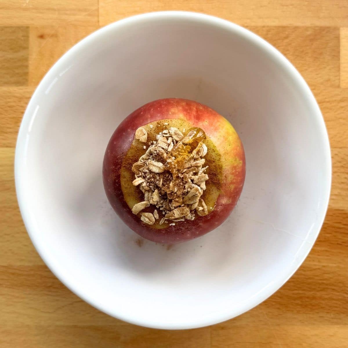 Whole apple stuffed with oats, cinnamon, and honey before microwaving in a bowl.