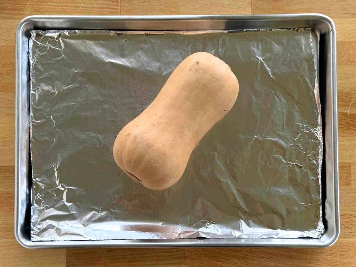 Whole butternut squash on a baking sheet ready to roast in the oven.