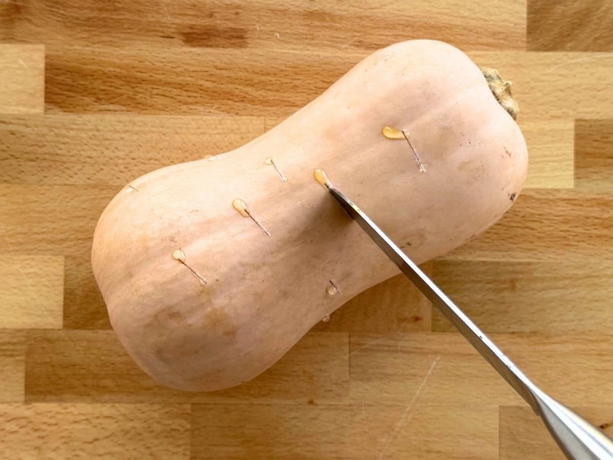 Piercing a whole butternut squash with a knife before cooking.