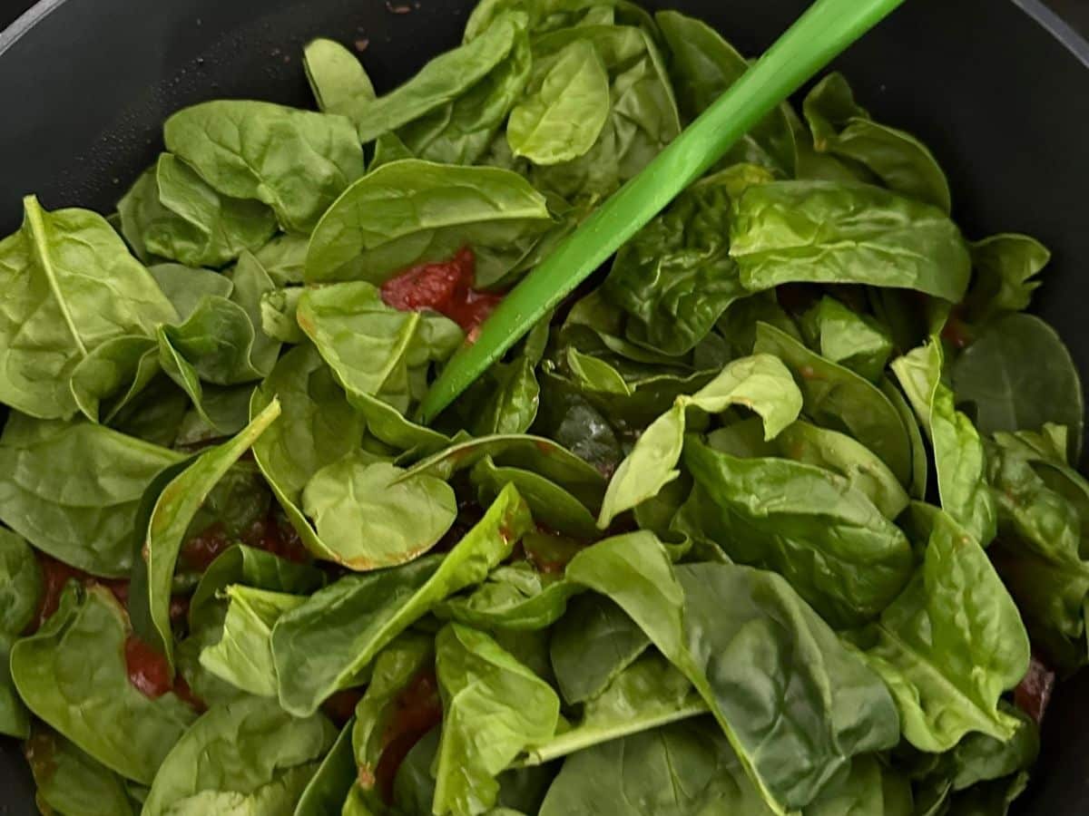 Fresh baby spinach leaves piled into a pot of tomato Florentine soup, ready to be stirred into the tomato base.