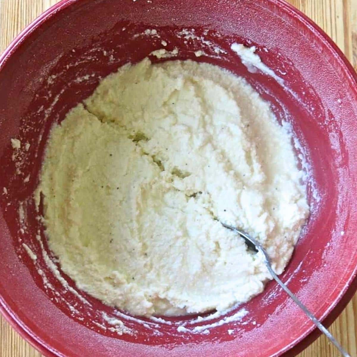 Ricotta, mozzarella, Parmesan, egg, salt, and pepper combined in a bowl with a spoon separating it into two halves.