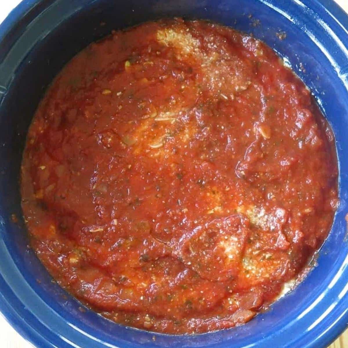 Assembled crockpot baked ziti topped with marinara before cooking and adding cheeses.