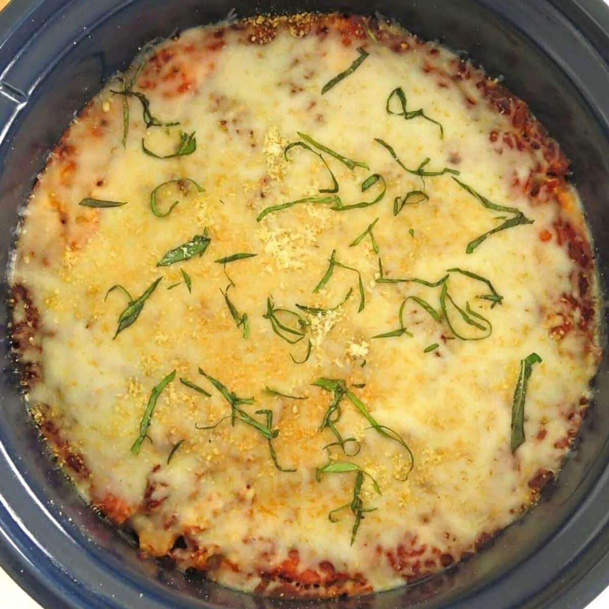 Finished crockpot baked ziti topped with melted mozzarella, Parmesan, and fresh basil.