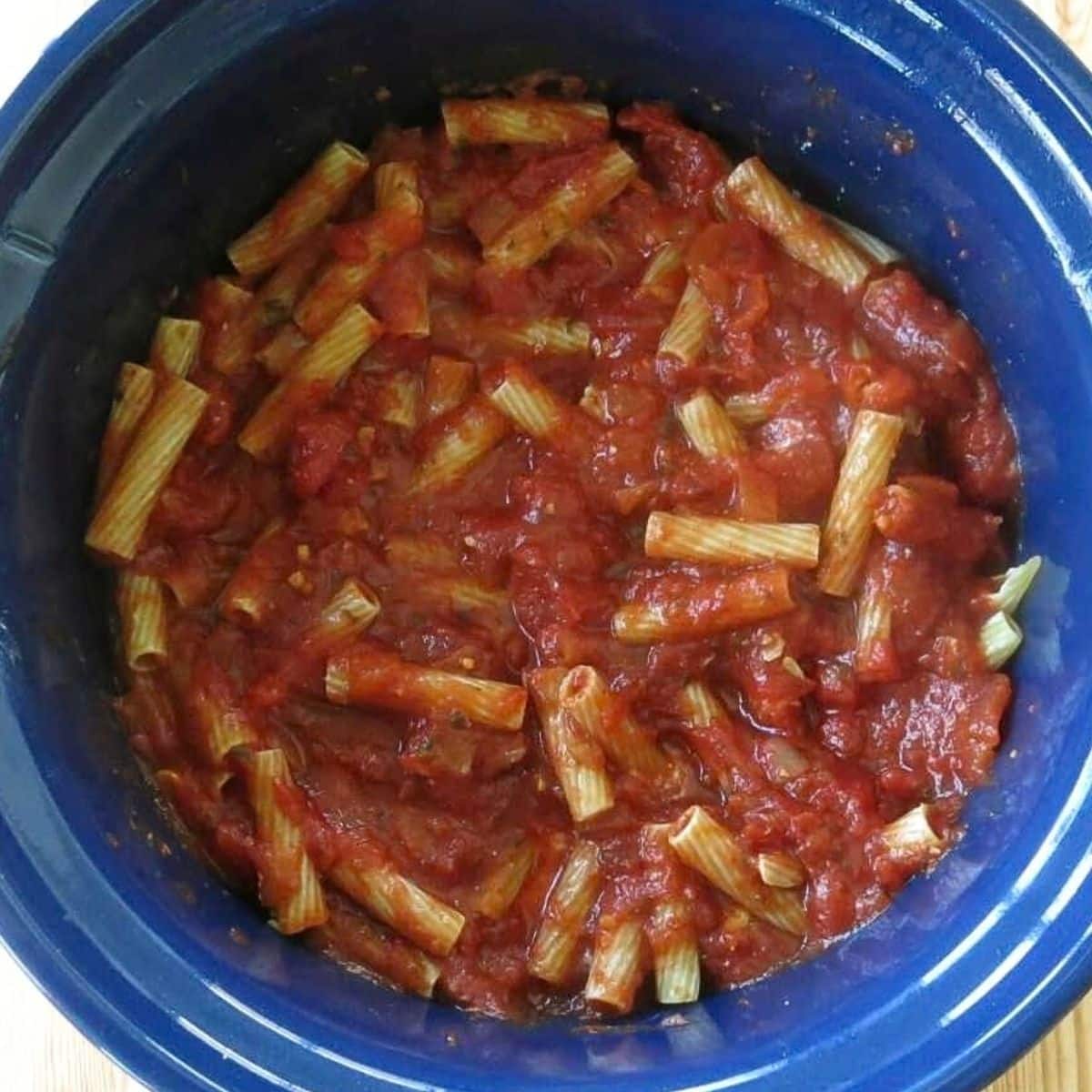 Uncooked ziti pasta coated with marinara in a slow cooker.