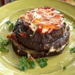 Eggplant Parmesan stack layered with marinara, mozzarella, and Parmesan on a green plate.