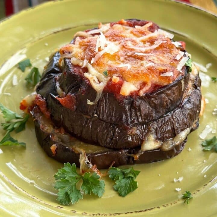 Eggplant Parmesan stack layered with marinara, mozzarella, and Parmesan on a green plate.