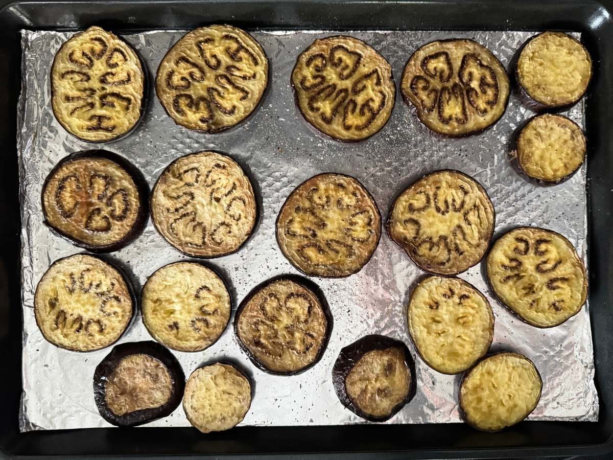 Roasted eggplant slices arranged on a foil-lined baking sheet.