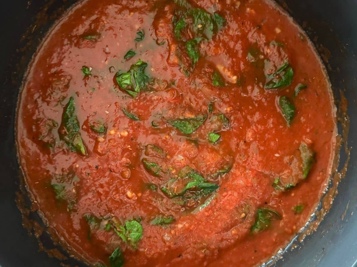 Tomato Florentine soup in a large pot with wilted spinach distributed throughout the thick, red tomato broth.