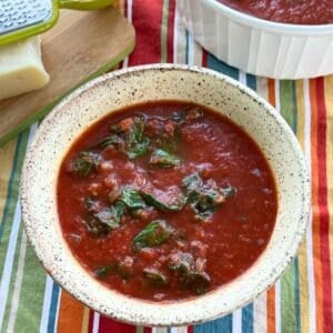 Bowl of tomato Florentine soup with a thick crushed tomato broth, wilted baby spinach, and diced onions, served on a colorful striped tablecloth.