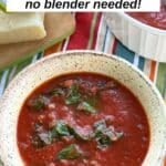 Bowl of tomato Florentine soup with a thick crushed tomato broth, wilted baby spinach, and diced onions, served on a colorful striped tablecloth